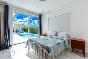 Un dormitorio con cama, mesita de noche, ventana grande y vista a una piscina.