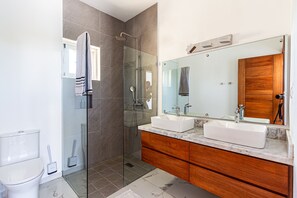 Un baño moderno con cabina de ducha de vidrio, un lavabo blanco y un mueble de tocador de madera.