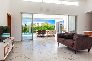 A modern living room with a sofa, TV, and a dining area with chairs. - Private Sosua Villa, Pool, BBQ, Sosua Ocean Village (Sosúa)