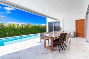 A modern dining area with a pool view, a large window, and a wooden door. - Private Sosua Villa, Pool, BBQ, Sosua Ocean Village (Sosúa)