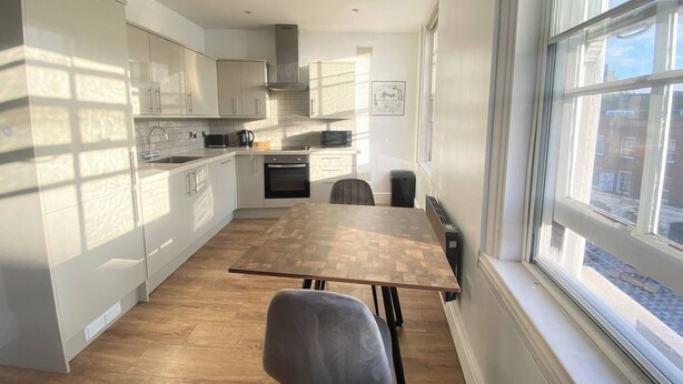 Una cucina moderna con mobili bianchi, un tavolo da pranzo in legno e vista attraverso una grande finestra.
