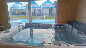 Ein Whirlpool mit Bedienfeld, Blick auf ein blaues Haus durch ein Fenster und eine Holzverkleidung.