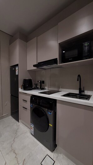 Eine kleine Küche mit Kühlschrank, Waschmaschine, Kaffeemaschine und Mikrowelle.