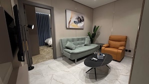Ein modernes Wohnzimmer mit einem grauen Sofa, einem orangefarbenen Sessel, einem kleinen runden Tisch und einem Gemälde an der Wand.
