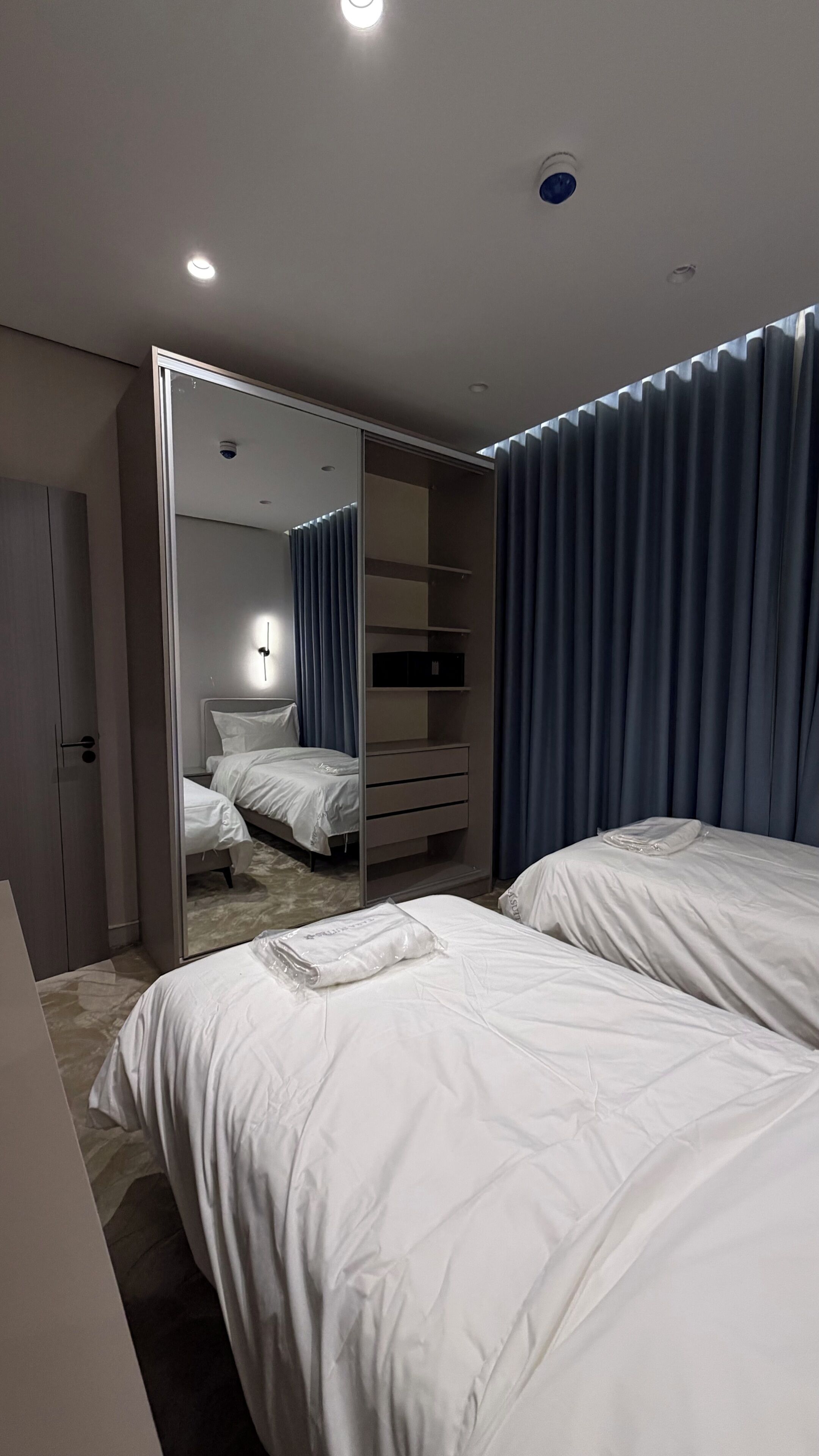 Een slaapkamer met twee bedden, een kledingkast, een spiegel en een plafondlamp.