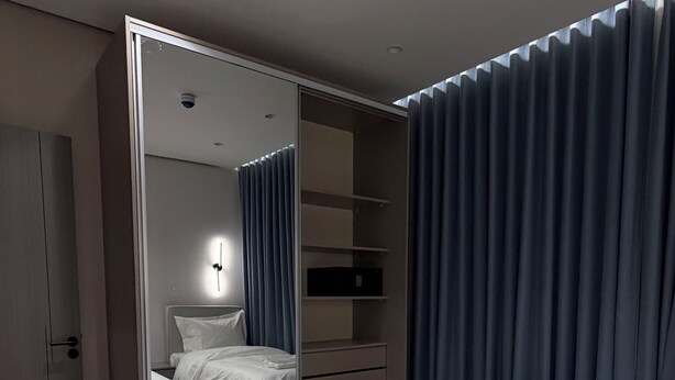 Ein Schlafzimmer mit zwei Betten, einem Kleiderschrank, einem Spiegel und einer Deckenleuchte.