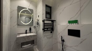 Un baño moderno con pared de mármol, un lavabo, un espejo con luz circular, un perchero y un cabezal de ducha manual.