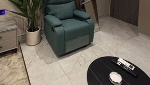 Una sala moderna con un sofá color turquesa, una planta en maceta, una mesa de centro negra y un área de cocina pequeña visible a través de un espejo.