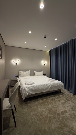 A hotel room with a bed, desk, chair, and two wall-mounted lights.