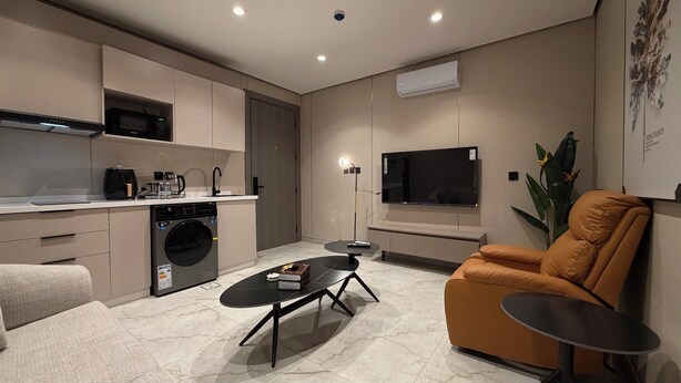 A modern kitchen with a built-in washing machine, a dining area with a round table, and a comfortable orange armchair. - 009 tara-JRE Jabal Al Lweibdeh with stunning view (Amman)