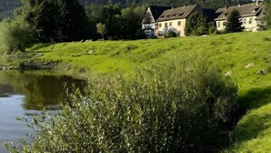 A lakeside property with a house, a pond, and a forested hill. - Apartment 'Alter Weserhof Forst' with Private Garden and Balcony (Bevern)
