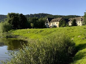 Ein See mit einer daran grenzenden Anlage, die ein Haus, einen Teich und einen bewaldeten Hügel umfasst.