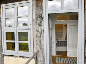 Ein Zimmer mit einem großen Fenster, einer Holztür und Blickrichtung auf ein Badezimmer.