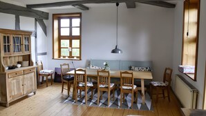 A dining area with a wooden table, chairs, a bench, a cabinet, and a window with blinds. - Apartment 'Alter Weserhof Forst' with Private Garden and Balcony (Bevern)