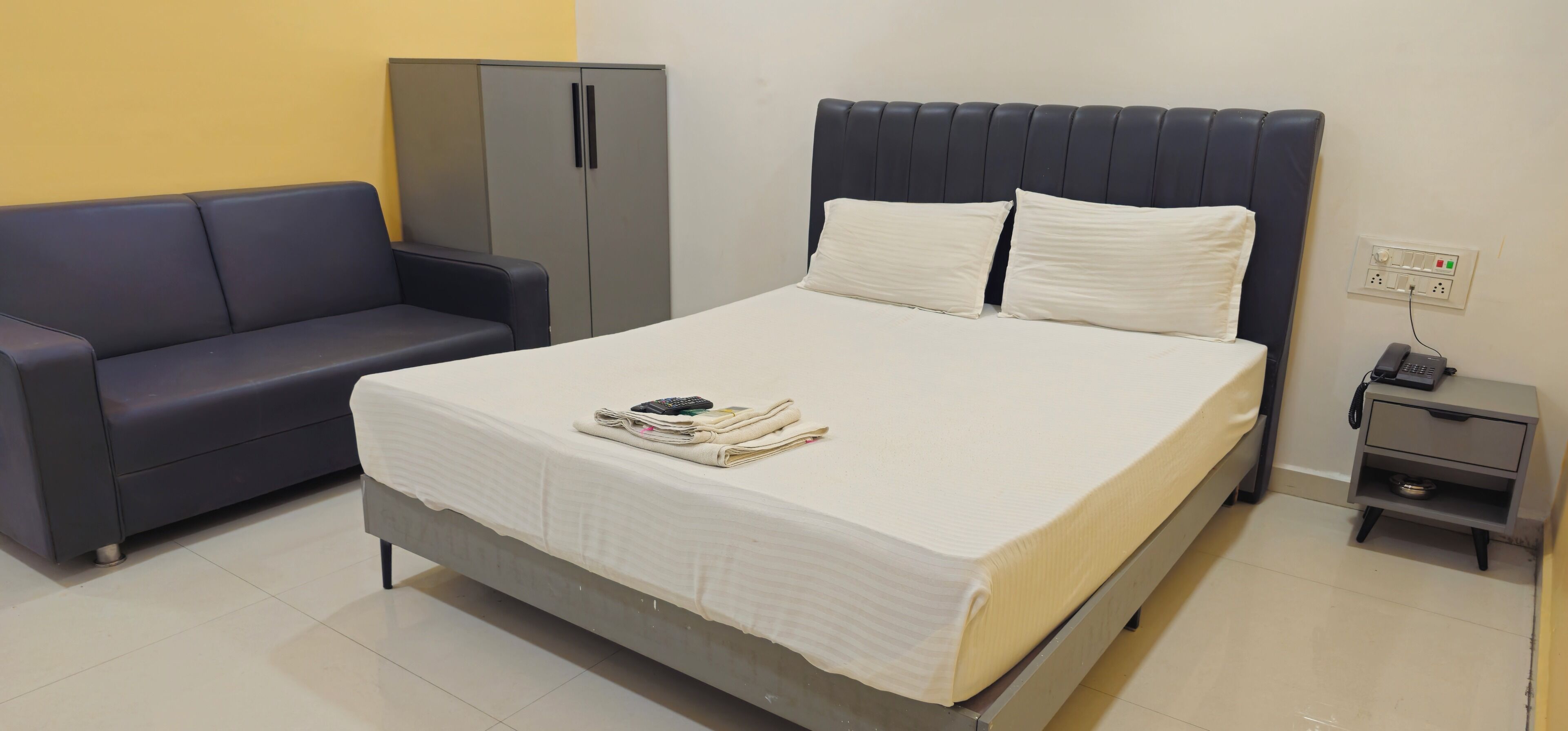 Una habitación de hotel con una cama, un armario gris, una mesita de noche gris y un sofá gris.