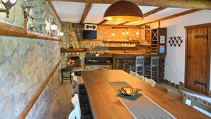 A rustic interior with stone walls, wooden beams, a long dining table, and a bar area with shelves and a television. - Klecherova House (Bansko)