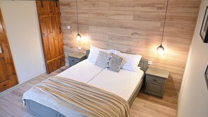 A bedroom with a bed, wooden wall paneling, two bedside tables, and hanging pendant lights. - Klecherova House (Bansko)