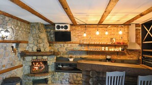 A rustic stone fireplace, wooden beams, a stone wall, a bar area with stools, and a television mounted on the wall. - Klecherova House (Bansko)