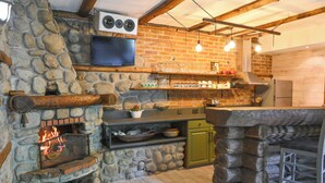 A stone fireplace with a TV above it, a stone wall, and a wooden ceiling. - Klecherova House (Bansko)