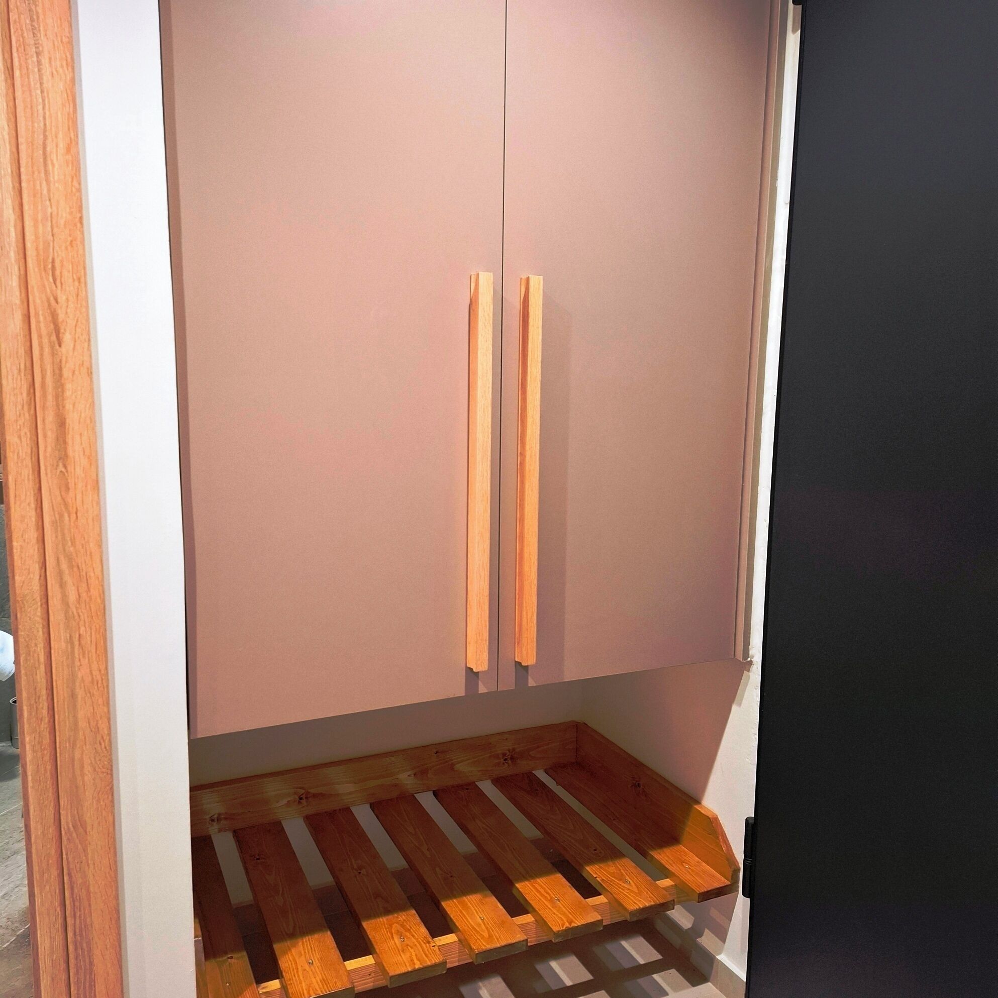 A room with a wooden floor, a pink cabinet with two handles, and a dark wall.