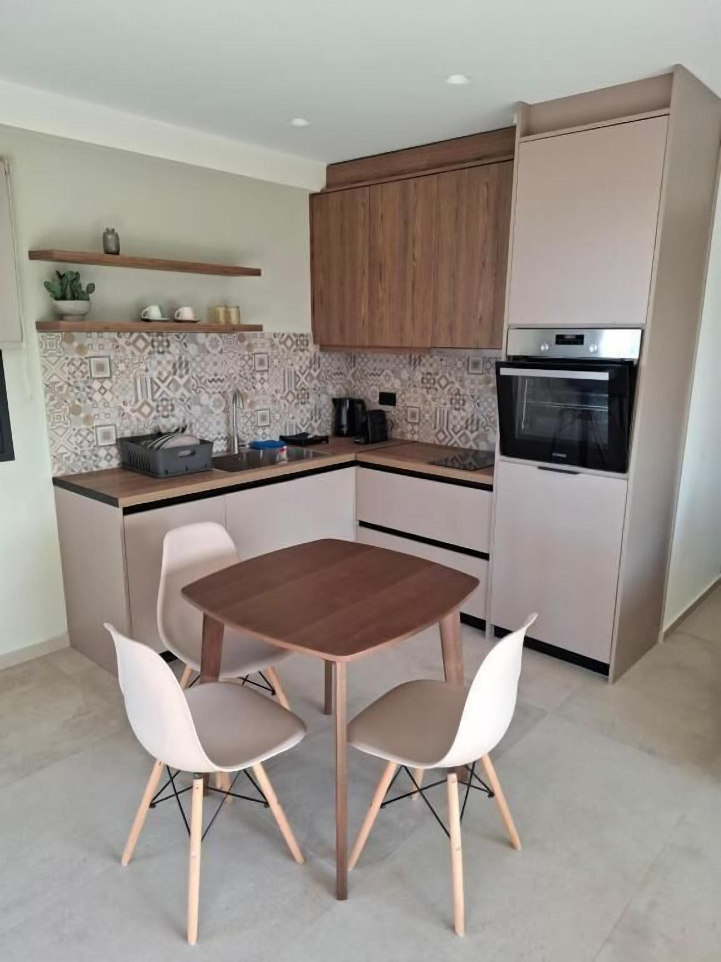 Una cocina moderna con una mesa y sillas de madera, horno empotrado y cafetera.