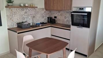 Una cocina moderna con una mesa y sillas de madera, horno empotrado y cafetera.