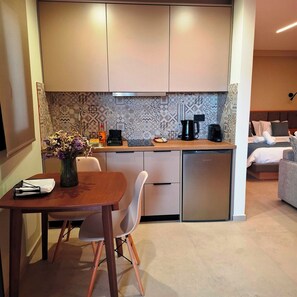 A compact kitchen with a dining area, a coffee machine, and a refrigerator. - Aelia Luxury Apartments & Pool (Skafidia)