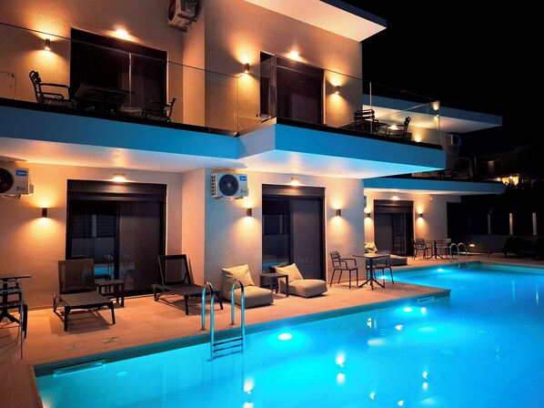 A modern hotel with a swimming pool, outdoor seating, and multiple balconies. - Aelia Luxury Apartments & Pool (Skafidia)