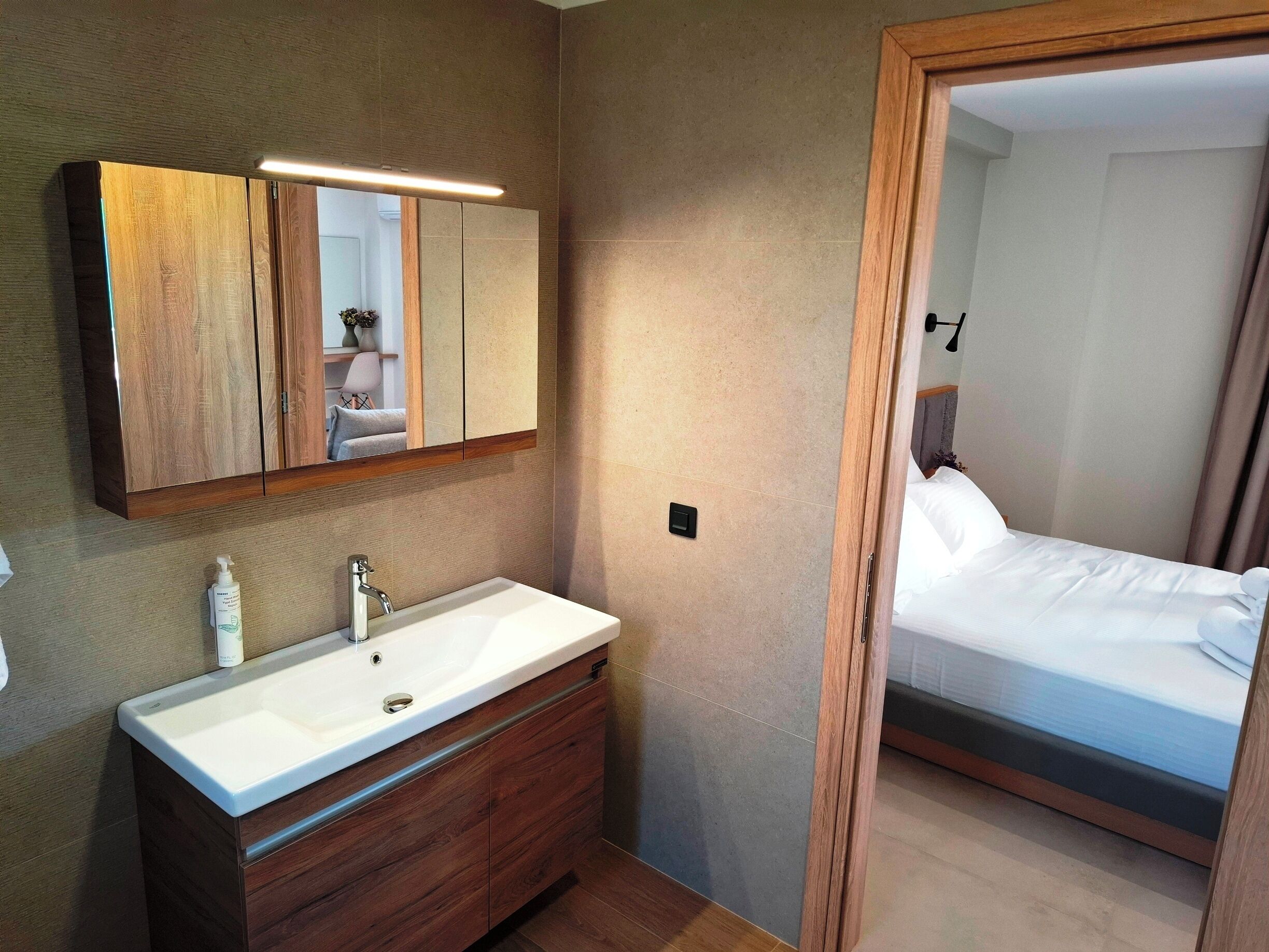 A modern bathroom with a wooden vanity, a large mirror, and a white sink.