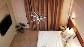 A hotel room with a bed, a TV, a wall-mounted air conditioner, a ceiling light fixture, and a small table with a remote control.