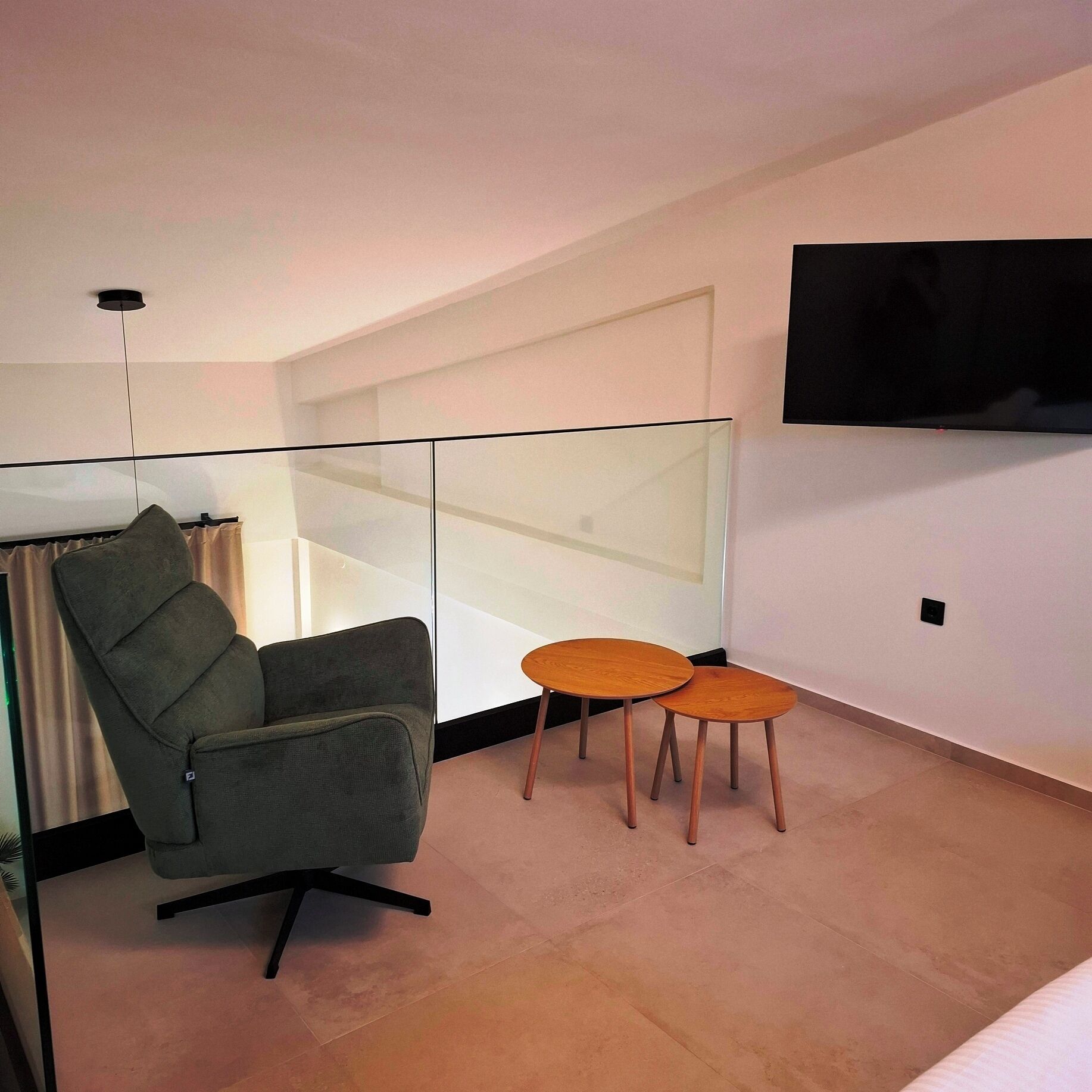 Quarto moderno com uma poltrona cinza, uma pequena mesa de madeira e uma TV fixada na parede.