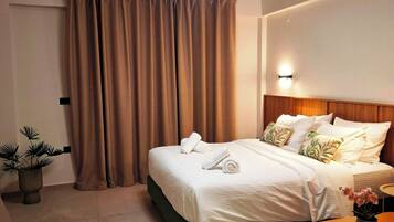 A hotel room with a bed, a bedside table, a potted plant, a wall-mounted air conditioner, and a modern ceiling light fixture.