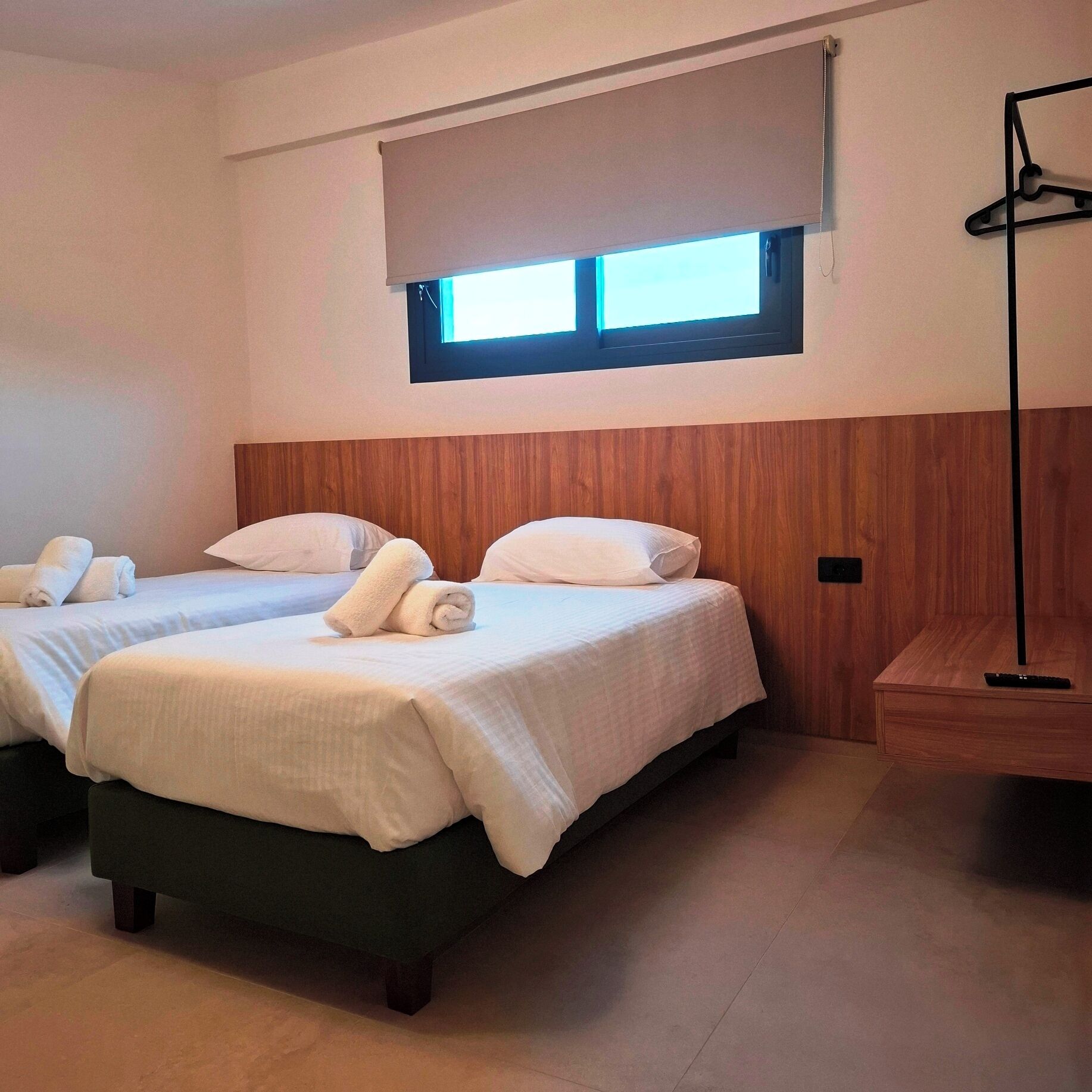 Een hotelkamer met twee bedden, een houten hoofdbord, een raam met zonwering en een staande lamp.