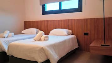 Een hotelkamer met twee bedden, een houten hoofdbord, een raam met zonwering en een staande lamp.