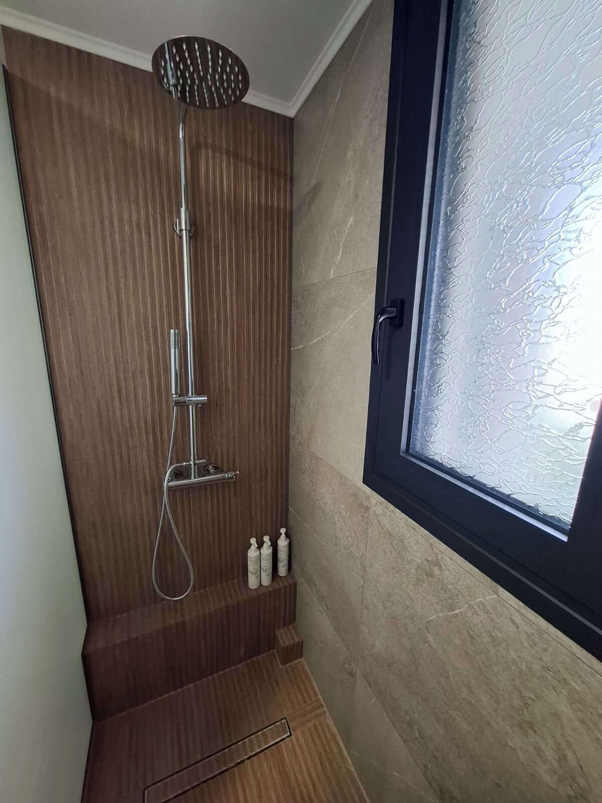 Een douche met een regendouche, een handdouche en een handmasseuse. Drie flessen shampoo en conditioner staan op de vloer.