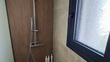 Een douche met een regendouche, een handdouche en een handmasseuse. Drie flessen shampoo en conditioner staan op de vloer.