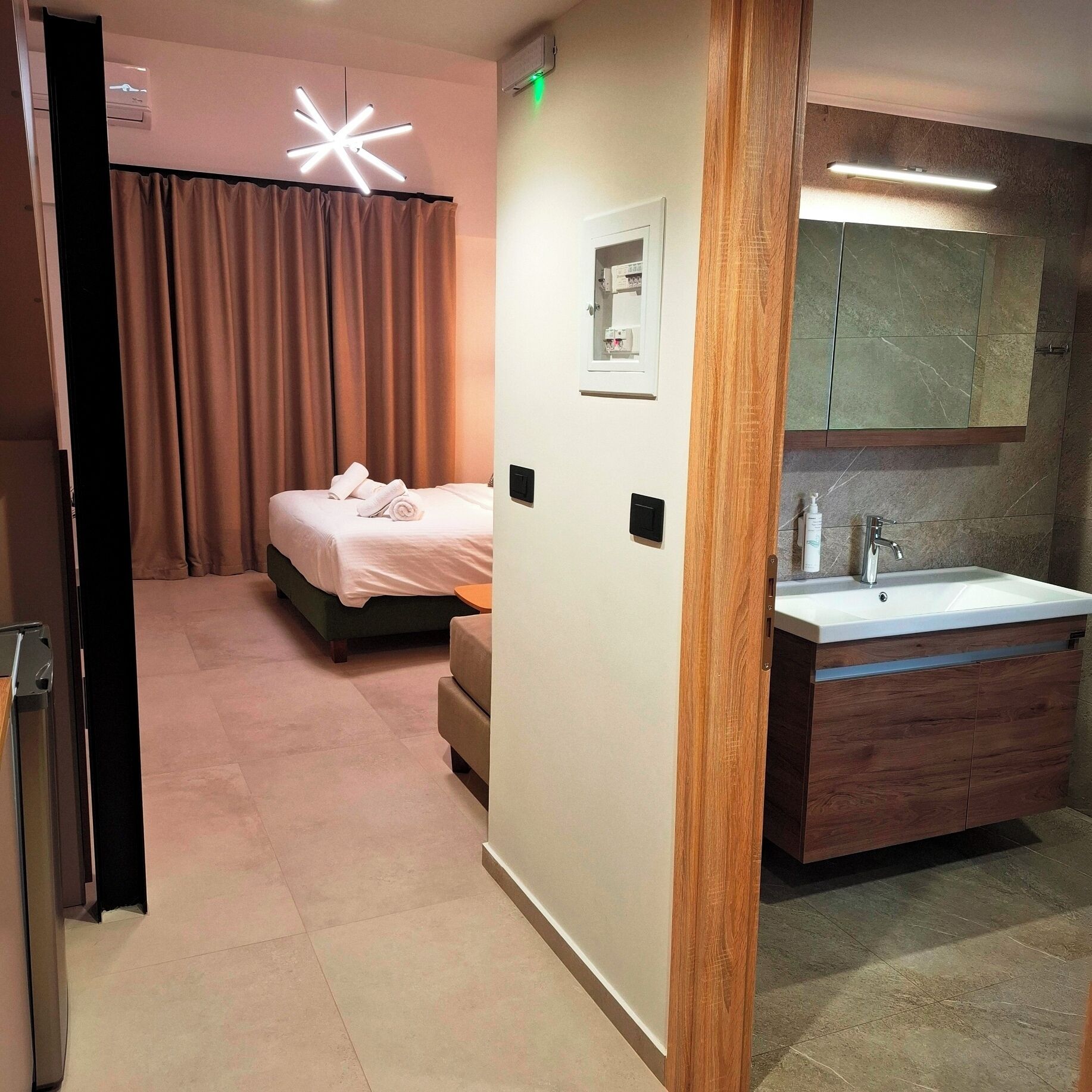 Habitación de hotel con cama, mesita de noche, baño con lavamanos y espejo, y una lámpara en forma de estrella.