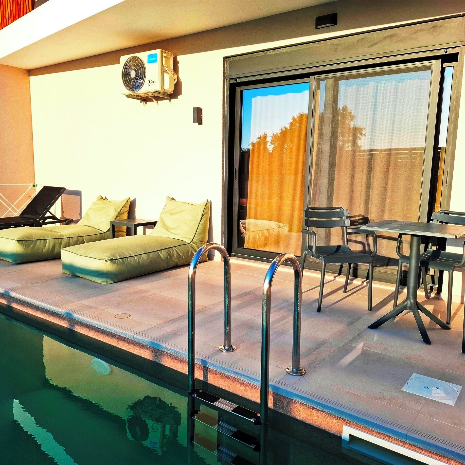 Un área junto a la piscina con sillones de descanso, una mesa y un ventilador de techo.