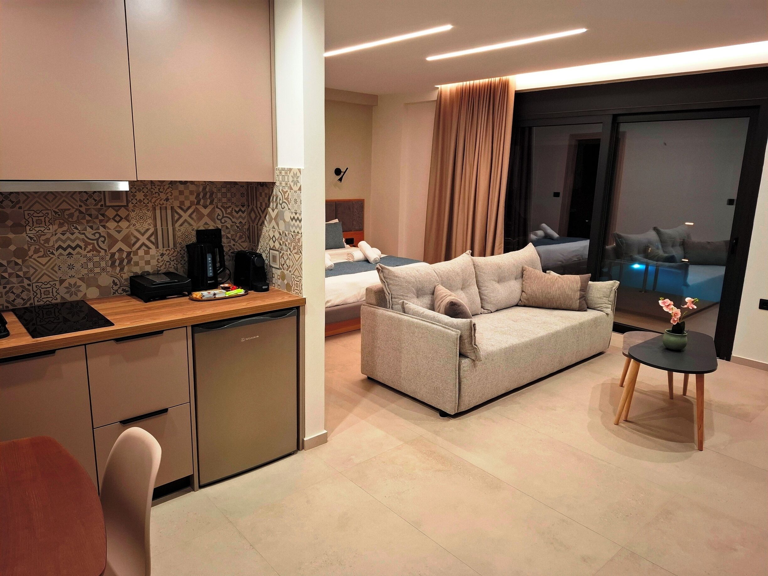 Ein modernes Hotelzimmer mit einer Küchenzeile, einem Sofa, einem kleinen Tisch und Blick ins Freie.