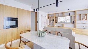 Une cuisine moderne avec des meubles en bois, un four encastré et un coin repas comprenant une table en marbre et des chaises en bois.