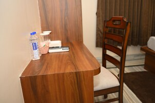 Un escritorio de madera con una silla, una botella de agua, un control remoto y una cesta pequeña.