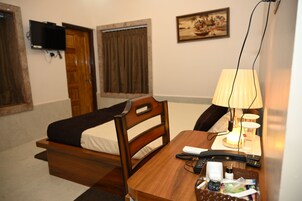 A hotel room with a bed, a desk with a lamp, a remote control, and a bottle.