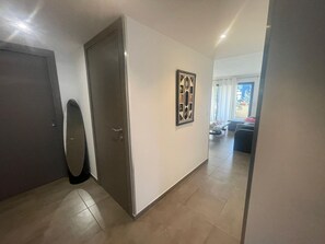 Ein Flur mit einer Tür, einem gerahmten Bild und Blick in einen Wohnbereich mit Sofa und Fenster.