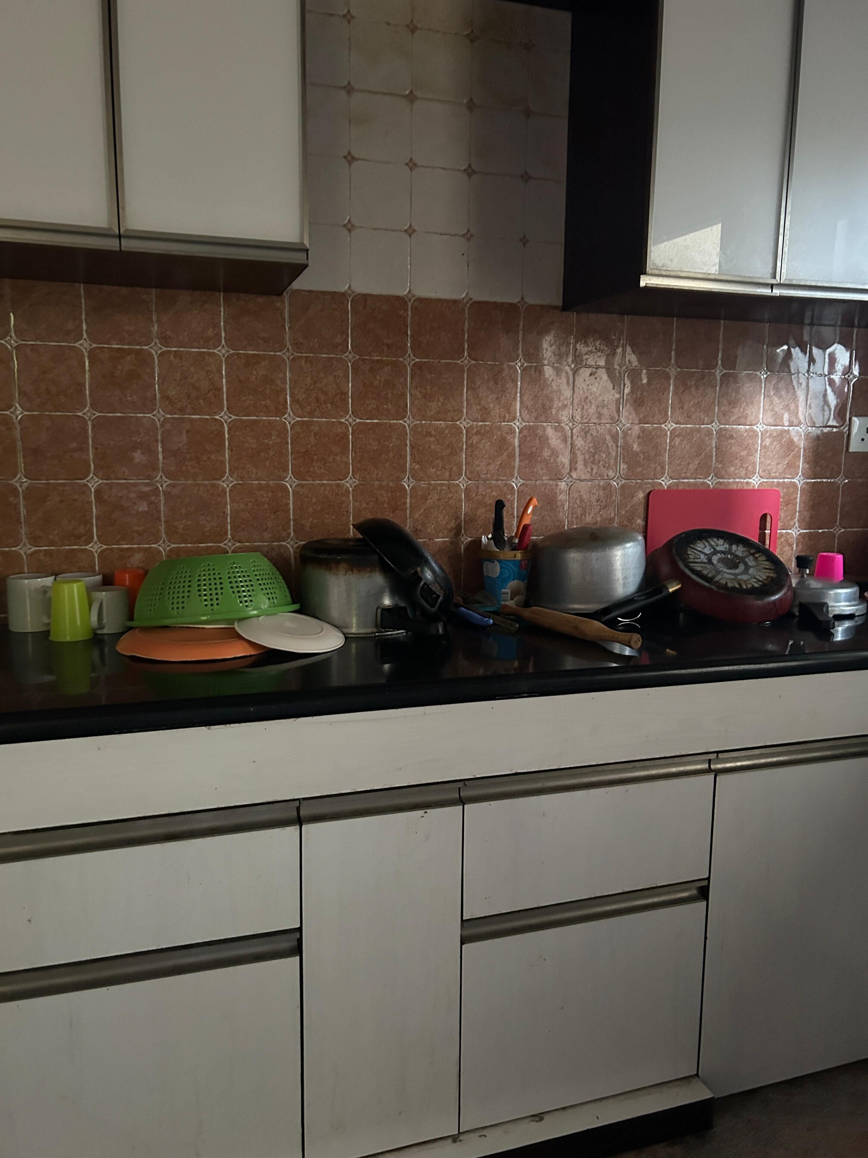 Une cuisine avec un mur recouvert de carreaux, un plan de travail sur lequel sont disposés divers ustensiles et accessoires de cuisine, et des armoires blanches.