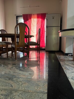A dining area with a table and chairs, a refrigerator, and a window with a red curtain. - Marvelous 3-bedroom apartment with AC in vibrant Chennai (Chennai)