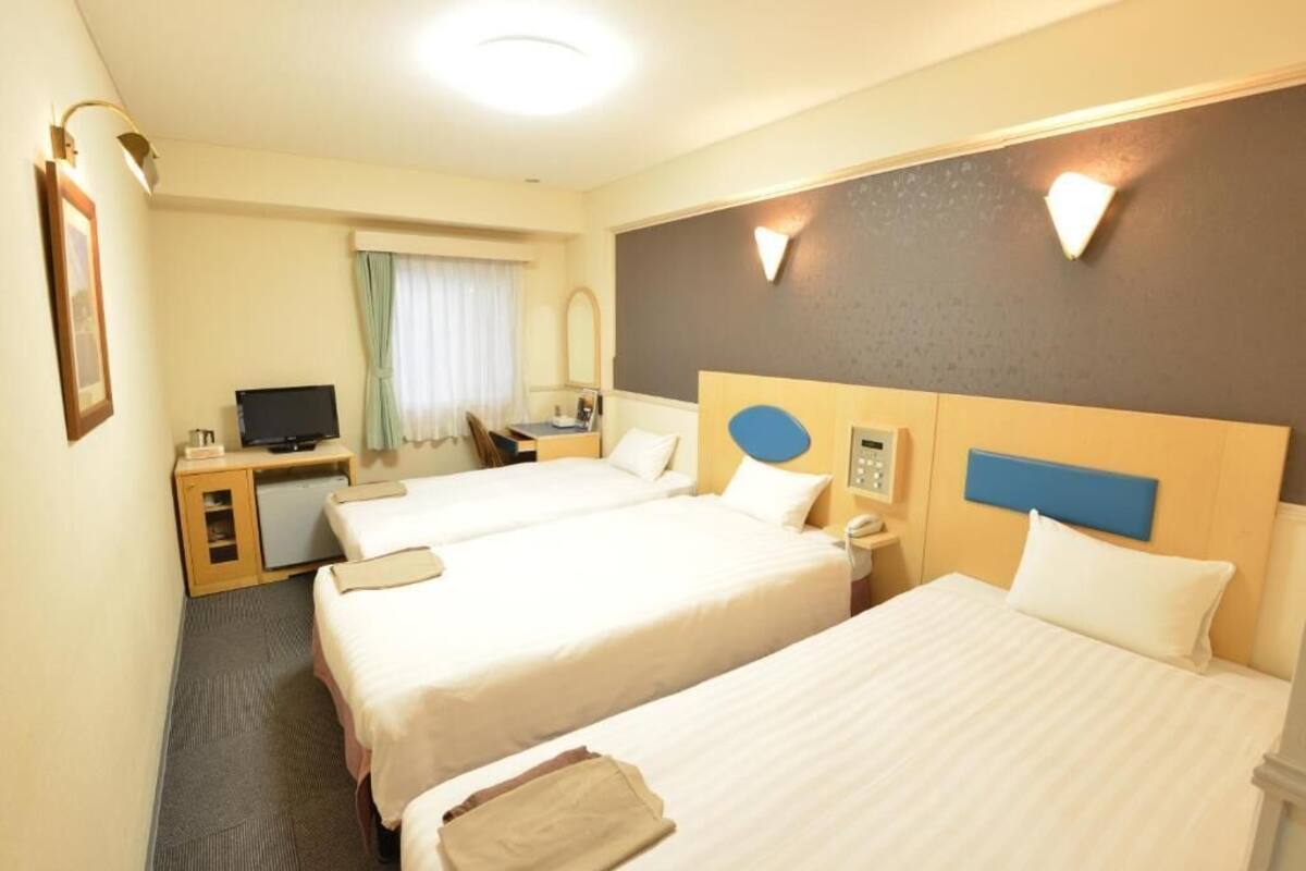 A hotel room with three beds, a desk with a computer, a telephone, and a mirror.