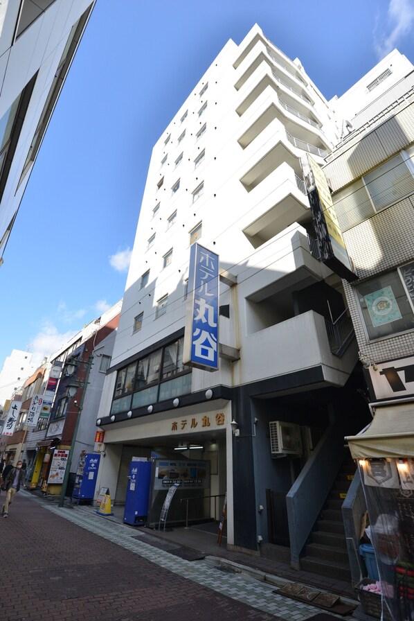 Un hôtel à plusieurs étages, reconnaissable à son grand panneau bleu, avec un escalier menant à l’entrée et un ciel bleu clair en arrière-plan.