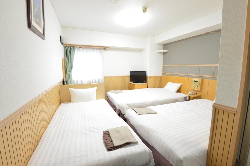 Une chambre d’hôtel avec deux lits simples, une télévision, une table de chevet et une fenêtre avec des rideaux.