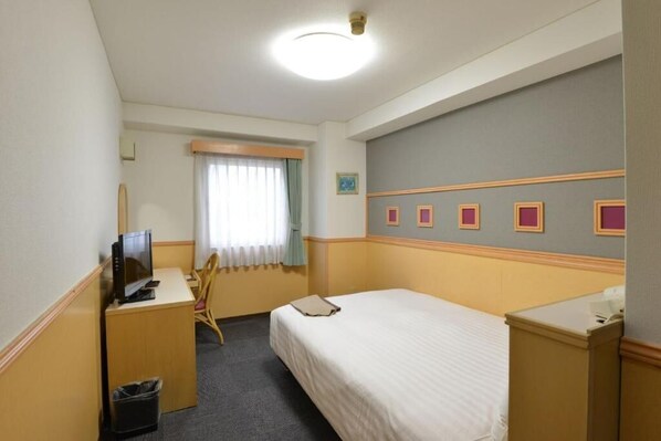 A hotel room with a bed, a desk with a computer, a chair, a small trash bin, and a window with curtains. - Hotel Marutani (Tokyo)