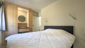 Makuuhuone, jossa on sänky, puinen vaatekaappi, pyöreä peili, yöpöytä ja seinään kiinnitetty lamppu.